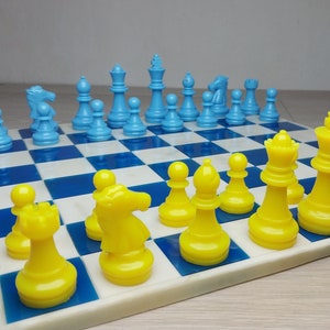 Peut inclure: Un jeu d'échecs bleu et jaune sur un échiquier blanc et bleu. Les pièces sont disposées dans une partie en cours.