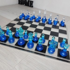 Peut inclure: Un jeu d'échecs en verre bleu et transparent sur un échiquier noir et blanc. Les pièces d'échecs sont disposées sur le plateau en position de départ.