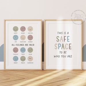 May include: Two framed prints with a light wood frame. The print on the left has a white background with colorful circles depicting different emotions. The text below the circles reads "All feelings are valid". The print on the right has a white background with the text "This is a safe space to be who you are".