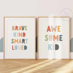 May include: Two framed art prints with inspirational words. One print says "BRAVE KIND SMART LOVED" in colorful letters. The other print says "AWESOME KID" in colorful letters. Both prints have a white background and a light wood frame.