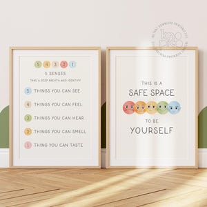 May include: Two framed prints with text and illustrations. One print lists the "5 Senses" with numbered items. The other print reads "This is a Safe Space to Be Yourself" with colourful smiley faces. Both are in light wood frames.