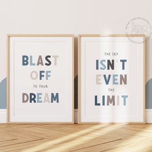 May include: Two framed prints with inspirational quotes. The left print reads "BLAST OFF TO YOUR DREAM" in blue, gray, and brown letters. The right print says "THE SKY ISN'T EVEN THE LIMIT" in similar colors. Both are in light wood frames.