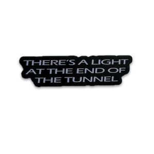 May include: Black rectangular sticker with rounded edges. The sticker features the white text: "THERE'S A LIGHT AT THE END OF THE TUNNEL". The sticker is set against a white background.