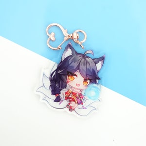 Pu&ograve; includere: Un portachiavi in acrilico trasparente con un personaggio di anime dei cartoni animati con lunghi capelli neri, un abito rosso e oro e un globo blu nella sua mano. Il personaggio ha orecchie da volpe e una coda bianca e soffice.