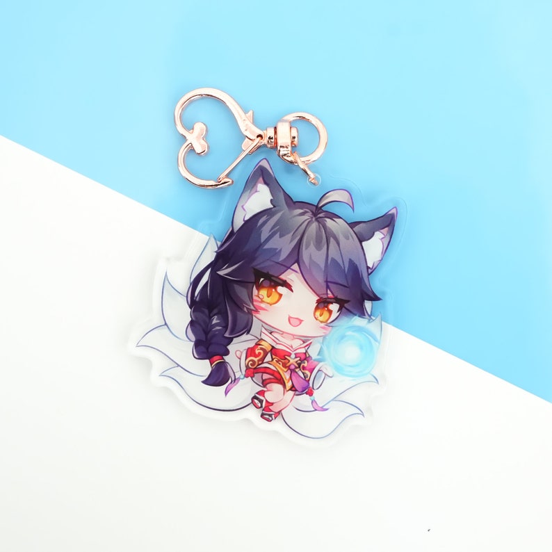 Pu&ograve; includere: Un portachiavi in acrilico trasparente con un personaggio di anime dei cartoni animati con lunghi capelli neri, un abito rosso e oro e un globo blu nella sua mano. Il personaggio ha orecchie da volpe e una coda bianca e soffice.