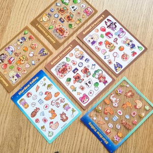 May include: A set of ten sticker sheets featuring characters from the video games Animal Crossing and Stardew Valley. The stickers are printed on clear vinyl and have a glossy finish. The sheets are packaged in clear plastic sleeves.