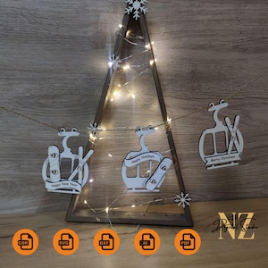 May include: A wooden Christmas tree with a triangular frame, decorated with fairy lights and snowflake ornaments. White ski lift-themed decorations with holiday greetings hang from the tree. The tree is set against a wooden background.