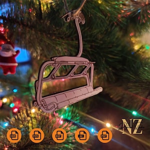 May include: A white wooden Christmas ornament shaped like a ski lift chair. The ornament is hanging from a Christmas tree with colourful lights.