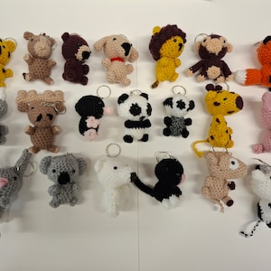 Może przedstawiać: Kolekcja 20 breloków z dzianych zwierząt. Breloki są wykonane w różnych kolorach i przedstawiają zwierzęta, takie jak lew, panda, żyrafa i krowa.