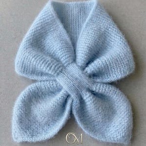 Puede incluir: Una bufanda de punto azul claro con un diseño único. La bufanda está hecha de hilo suave y esponjoso y presenta un centro anudado y extremos acampanados. El nombre del diseñador, Olga Mokrousova, está impreso en la parte inferior de la imagen.