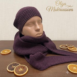 May include: A dark purple knitted beanie with a ribbed brim and a matching dark purple knitted scarf. The text Olga Mokrousova is visible in the upper right corner. The set is displayed on a mannequin head, with dried orange slices nearby.