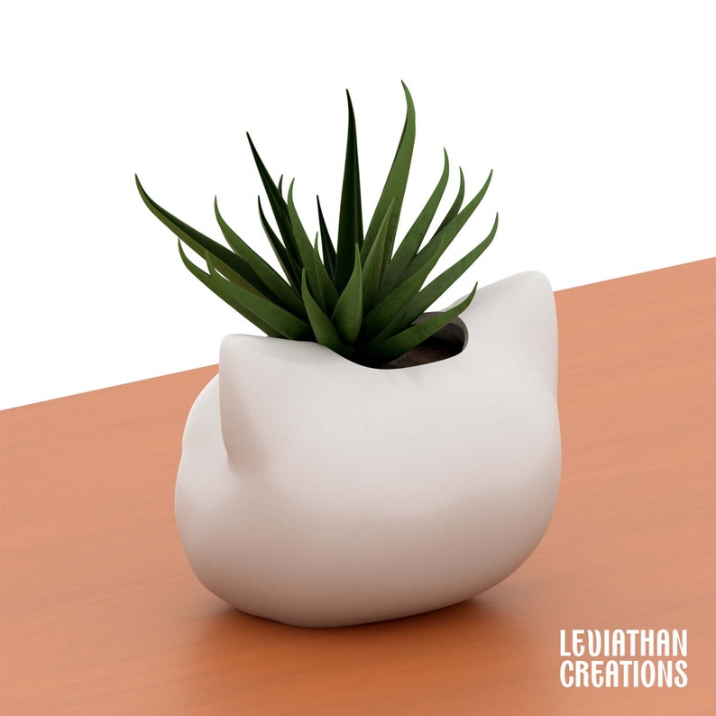May include: White ceramic planter shaped like a cat's head with a green succulent plant inside.