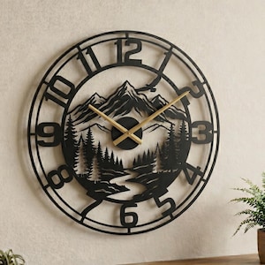 Könnte beinhalten: Schwarze Metall-Wanduhr mit Berg- und Waldlandschaft. Die Uhr hat ein kreisförmiges Design mit großen Ziffern und goldfarbenen Zeigern. Das Zifferblatt zeigt eine Bergkette, Bäume und einen Fluss.