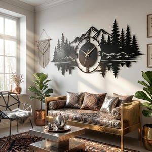 Puede incluir: Un gran reloj de pared de metal negro con la silueta de una cordillera y un bosque de pinos. La esfera circular está centrada en el diseño del paisaje y muestra manecillas doradas para las horas, los minutos y los segundos.