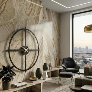 May include: A large, black metal wall clock with gold hands is mounted on a marble-effect wall. The clock has a circular frame with intersecting lines. The room features modern furniture and decor, including vases and a potted plant.