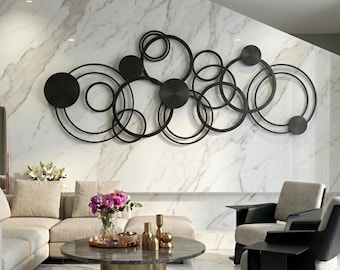 May include: A large, horizontal wall art piece composed of interconnected black metal rings and solid circular discs. The design features a complex arrangement of overlapping circles of varying sizes, creating an abstract geometric pattern mounted on a wall.