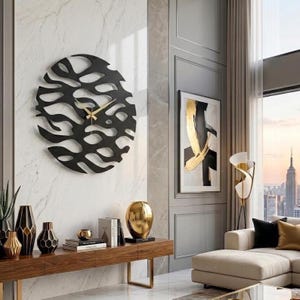 May include: A black, circular wall clock with a unique, openwork design. The clock features gold-colored hands and is mounted on a marble-patterned wall. The clock is a decorative element in a modern living room setting.