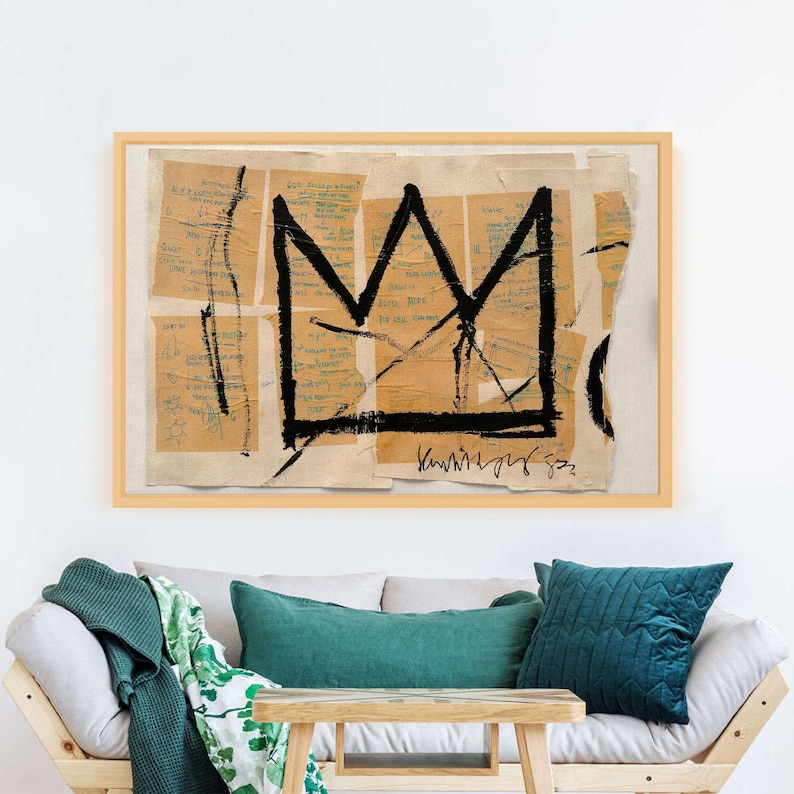 Puede incluir: Obra de arte enmarcada con un dise&ntilde;o de corona negra sobre un collage de fragmentos de papel beige con notas manuscritas. La obra est&aacute; en un marco de madera clara. Se exhibe sobre un sof&aacute; de madera clara con cojines verde azulado y una manta verde.