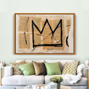 Puede incluir: Impresi&oacute;n art&iacute;stica abstracta con un dise&ntilde;o de corona negra sobre un fondo de fragmentos de papel rasgados con texto manuscrito. La obra de arte est&aacute; enmarcada en un marco de madera marr&oacute;n. La pieza se exhibe sobre un sof&aacute; blanco con cojines verdes y estampados.