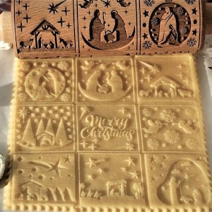 Peut inclure: Un rouleau à pâtisserie en bois avec un motif de scène de la Nativité de Noël. Le rouleau à pâtisserie est utilisé pour créer des motifs décoratifs sur les biscuits. Le motif comprend une crèche, des étoiles et les mots "Joyeux Noël".