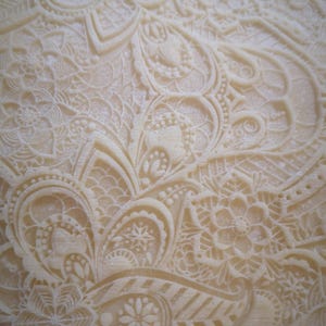 May include: Close-up of a white fondant cake with an intricate, embossed design. The design features a repeating pattern of swirls, leaves, and flowers.