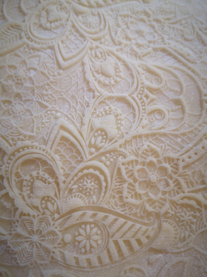 May include: Close-up of a white fondant cake with an intricate, embossed design. The design features a repeating pattern of swirls, leaves, and flowers.