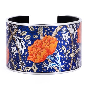 Puede incluir: Un brazalete de plata con un patrón floral azul y naranja. El diseño presenta flores y hojas estilizadas.