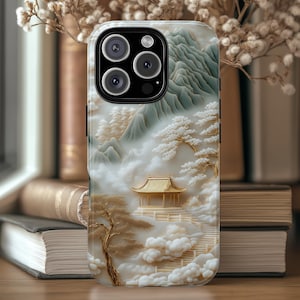 May include: A white and gold phone case with a detailed design of a mountain landscape, a pagoda, and clouds. The case has a camera lens cutout and a black border.