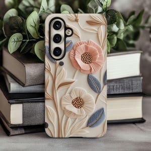 May include: A white phone case with a floral design. The flowers are pink and white and have a 3D effect. The case has a cutout for the camera lens.