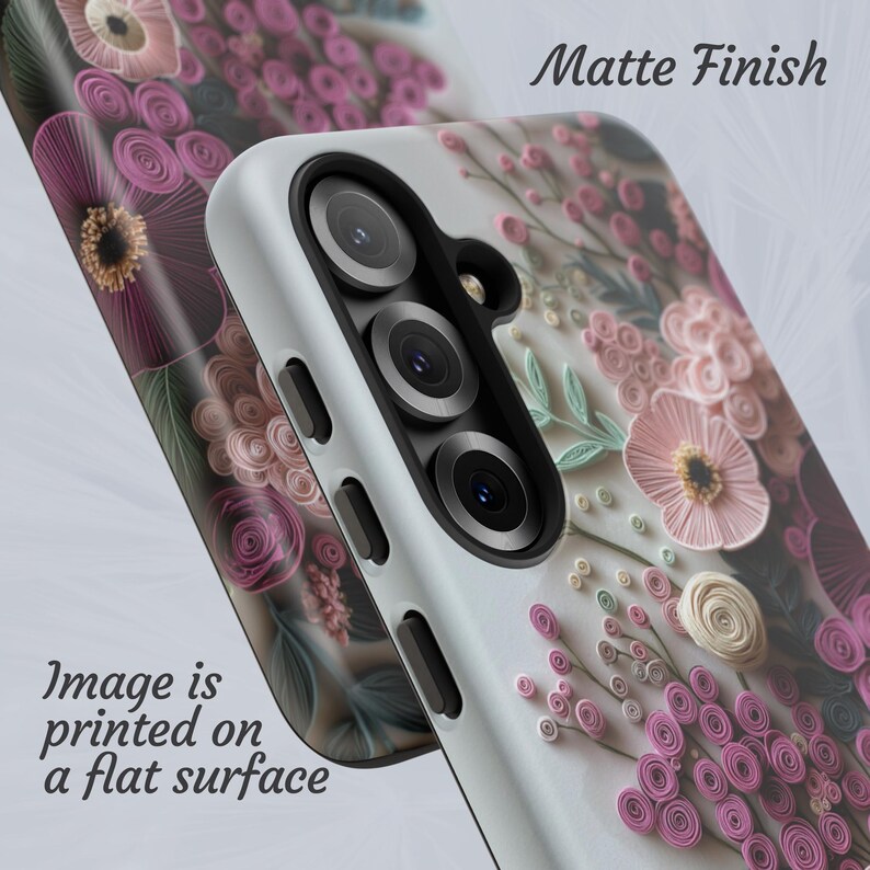 Puede incluir: Una funda de tel&eacute;fono con acabado mate, con un dise&ntilde;o floral en tonos rosa, morado y blanco. La imagen est&aacute; impresa sobre una superficie plana. La funda tiene una c&aacute;mara y botones.