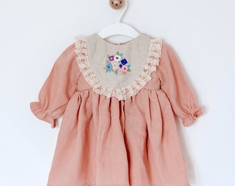 May include: A pink linen dress with a lace trim and embroidered flowers on the bodice.