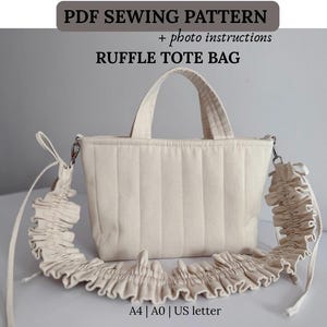 May include: A PDF sewing pattern for a ruffle tote bag with photo instructions. The image shows a cream-coloured quilted tote bag with two top handles and a long, detachable shoulder strap featuring a ruffled fabric design. A4, A0, US letter.