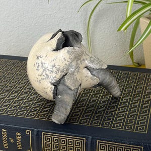 May include: A set of three ceramic mugs with a speckled, matte finish. The mugs are in shades of cream, light gray, and dark gray. Each mug has a simple, minimalist design and a rounded handle.