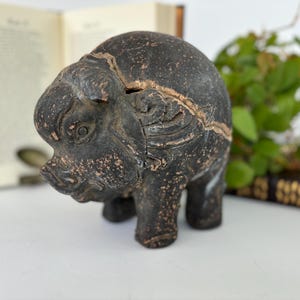 May include: A dark brown, hand-carved wooden pig figurine. The pig has detailed features and a textured surface.