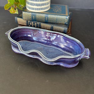 May include: A purple and blue ceramic planter with a wavy rim and two handles. The planter is sitting on a stack of books.