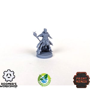 May include: A gray 3D printed miniature of a female wizard holding a staff with a skull at the top. The wizard is wearing a long robe and has a flowing cape. The miniature is standing on a round base.