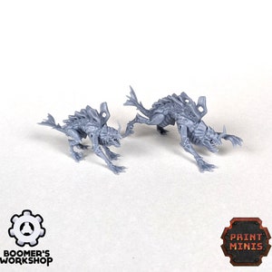 May include: Two grey 3D printed miniature figures of alien creatures with detailed sculpting. The figures are posed in a running stance with their mouths open and teeth visible. The larger figure is in the background and the smaller figure is in the foreground.