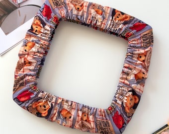 May include: A square fabric embroidery hoop cover featuring a repeating pattern of teddy bears, red hearts, and plaid sections with the text "TEDDY AND ME" printed in a dark font. The cover has an elasticized edge for a snug fit around a frame.
