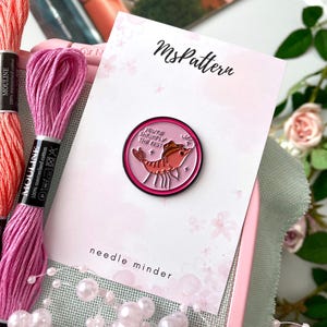 Könnte beinhalten: Ein rosa Nadelhalter mit einer Cartoon-Garnele mit Cowboyhut und dem Text "YOU'RE SHRIMPLEY THE BEST". Das Bild zeigt auch rosa Stickgarn und ein Kreuzstichprojekt.