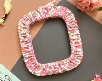 May include: A floral print hair curler in pink and white, with a square shape. The image also shows yellow and pink embroidery floss, gold scissors, and a magazine with the text "Cherish Friendship".