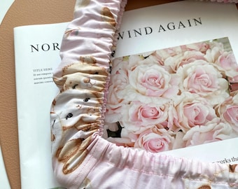 May include: Pink fabric chair cover with a white elastic band. The fabric has a pattern of brown bears and pink roses. The text "WIND AGAIN" is visible on the background.