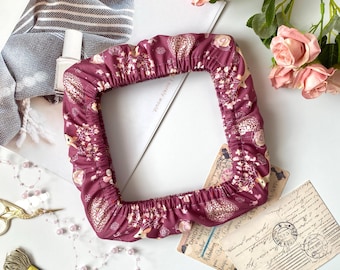 Puede incluir: Una funda de tela burdeos de forma cuadrada con un estampado floral y animal repetido. La funda está fruncida en los bordes. La imagen incluye rosas rosas, postales antiguas y material de costura.