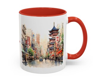 May include: White ceramic mug with a red rim and handle. The mug features a watercolor illustration of a street scene in a city with a pagoda-style building in the background. The street is lined with buildings and trees, and there are people walking on the sidewalk.