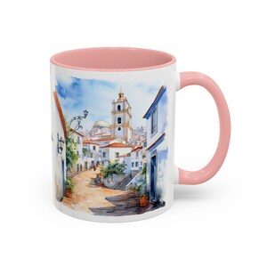 May include: White ceramic mug with a pink interior and a colorful watercolor illustration of a white-washed village with a church in the background.