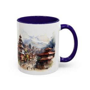 May include: White ceramic mug featuring a watercolour illustration of a cityscape with red-roofed buildings and mountains. The interior and handle are a deep blue colour. A decorative coffee mug.