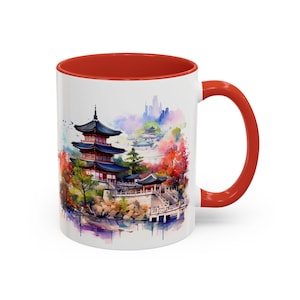 May include: White ceramic mug with a red interior and handle. The mug features a watercolor painting of a Japanese pagoda and surrounding landscape in shades of red, blue, and green.