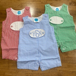 May include: Three gingham baby overalls in red, blue, and green. The blue overalls have a white oval patch with the monogram "HGN" embroidered in blue.