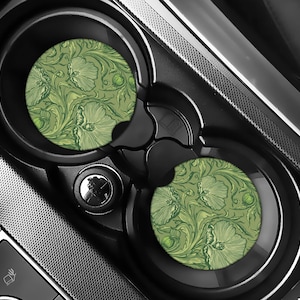 May include: Two car coasters with a green floral design, set inside a black car console. The coasters feature a repeating pattern of stylized flowers and leaves in shades of green, set against a lighter green background.