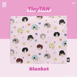 May include: A pink fleece blanket with a repeating pattern of cartoon faces and hearts. The faces are of different colors and have different expressions. The text "TinyTAN" is printed in black at the top of the image and the word "Blanket" is printed in black at the bottom of the image.