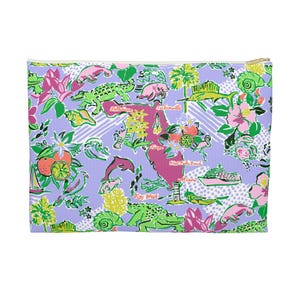 Könnte beinhalten: Eine rechteckige, lavendelfarbene Reißverschlusstasche mit einem farbenfrohen Florida-Themen-Druck. Das Design umfasst Illustrationen von Alligatoren, Delfinen, Blumen und Orangen mit Städtenamen wie Miami und Key West. Der Reißverschluss ist goldfarben.